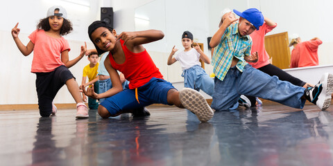 Multiethnic group of children in casual wear training hip hop movements in dance class with female coach..