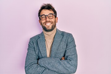 Handsome man with beard wearing business jacket and glasses happy face smiling with crossed arms looking at the camera. positive person.