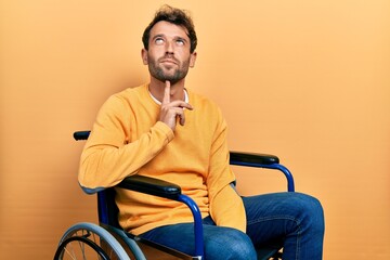 Handsome man with beard sitting on wheelchair thinking concentrated about doubt with finger on chin and looking up wondering