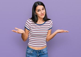 Young hispanic girl wearing casual striped t shirt clueless and confused expression with arms and...