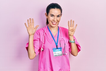Young brunette woman wearing doctor uniform and stethoscope showing and pointing up with fingers...