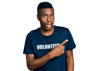 Young african american man wearing volunteer t shirt surprised pointing with finger to the side, open mouth amazed expression.