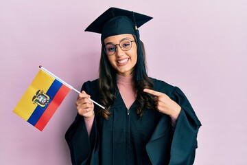 Young hispanic woman wearing graduation uniform holding ecuador flag smiling happy pointing with hand and finger