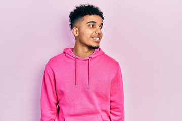 Young african american man wearing casual sweatshirt looking away to side with smile on face, natural expression. laughing confident.