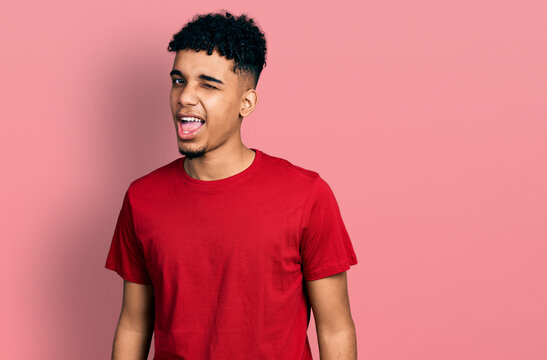 Young African American Man Wearing Casual Red T Shirt Winking Looking At The Camera With Sexy Expression, Cheerful And Happy Face.