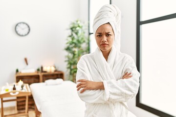 Young brunette woman wearing towel and bathrobe standing at beauty center skeptic and nervous, disapproving expression on face with crossed arms. negative person.