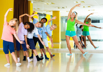 positive children dancing synchronous group choreography with female coach in dance hall