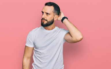 Young man with beard wearing casual white t shirt confuse and wondering about question. uncertain...