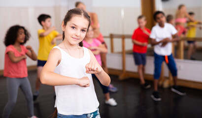 Fototapeta na wymiar Sporty ten years old girl training movements of vigorous dance during group class in dance school..