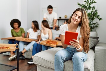 Group of young friends eating italian sitting on the sofa. Woman smiling and using touchpad at home.