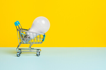 Light bulb in the toy Shopping cart or trolley on bright yellow background. Electricity sale or eco...