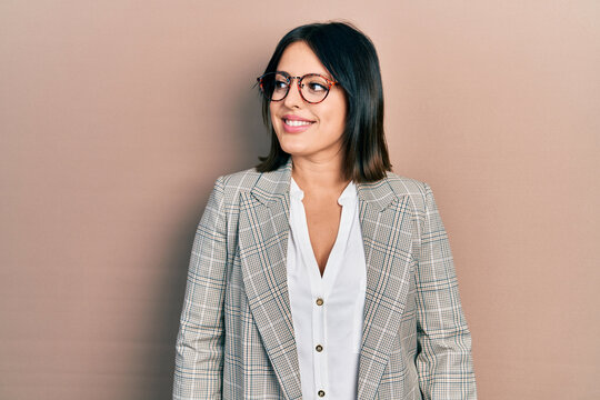 Young hispanic woman wearing business clothes and glasses looking away to side with smile on face, natural expression. laughing confident.