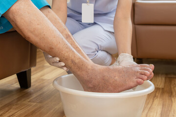 A female nurse is washing the feet of an old man for treatment preparation.