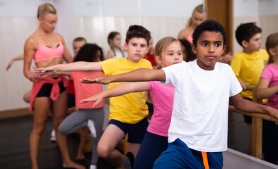 Fototapeta na wymiar Focused children standing along ballet bar in dance studio during class