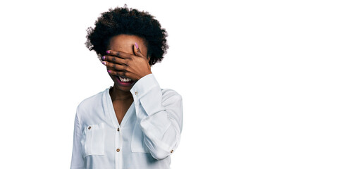 African american woman with afro hair wearing casual white t shirt smiling and laughing with hand on face covering eyes for surprise. blind concept.