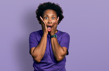 African american woman with afro hair wearing casual purple t shirt afraid and shocked, surprise and amazed expression with hands on face