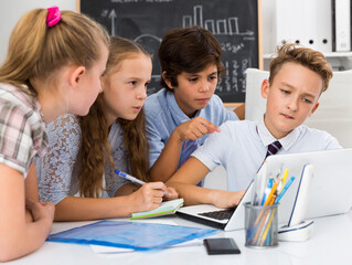Teens male and female discussing at the notebook near blackboard