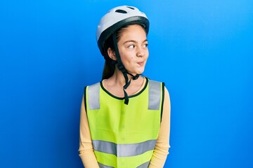 Beautiful brunette little girl wearing bike helmet and reflective vest smiling looking to the side and staring away thinking.