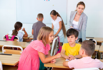 Fototapeta premium Preteen schoolchilds working in groups at lesson in primary school with teacher on background
