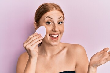 Young irish woman holding makeup sponge celebrating achievement with happy smile and winner expression with raised hand