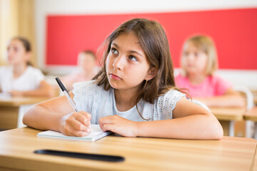 Portrait of cute intelligent schoolgirl who writing exercises at lesson in primary school