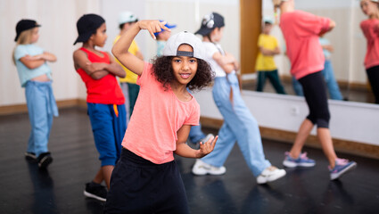 Smiling curly preteen girl dancing hip hop during group dance class for children