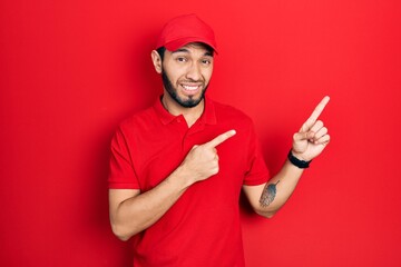 Hispanic man with beard wearing delivery uniform and cap pointing aside worried and nervous with both hands, concerned and surprised expression