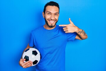 Hispanic man with beard holding soccer ball smiling cheerful showing and pointing with fingers teeth and mouth. dental health concept.