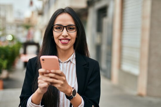 Young hispanic businesswoman smiling happy using smartphone at the city.
