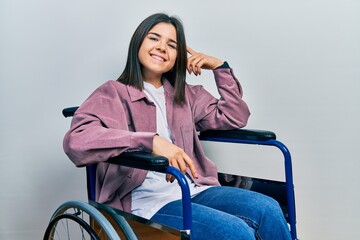 Young brunette woman sitting on wheelchair smiling pointing to head with one finger, great idea or thought, good memory