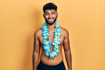 Arab man with beard wearing swimsuit and hawaiian lei looking positive and happy standing and...