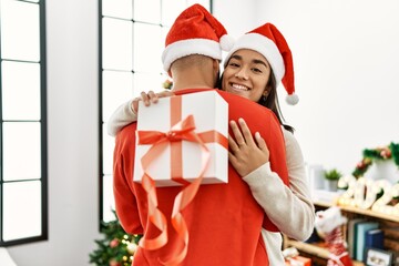 Young latin couple smiling happy and hugging holding christmas gift at home.