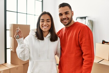 Young hispanic couple smiling happy holding key of new home.