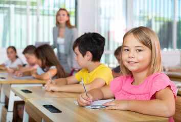 Fototapeta premium Kids studying in classroom. Girl sitting at desk and looking in camera.