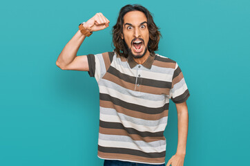 Young hispanic man wearing casual clothes angry and mad raising fist frustrated and furious while...