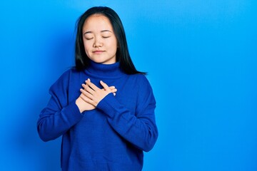 Young chinese girl wearing casual clothes smiling with hands on chest with closed eyes and grateful gesture on face. health concept.