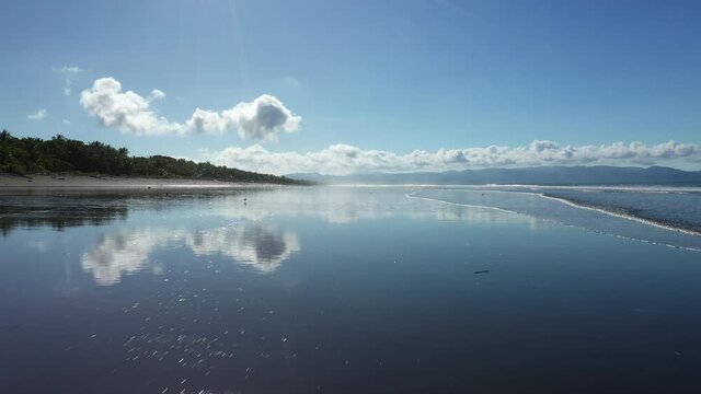 low aerial flight over black sandy beach water mirror reflection over playa Zancudo Costa Rica