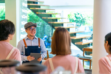 Asian male coffee shop manager briefing man and woman staff team before working. Small business cafe and restaurant owner instruct part time employee preparing service to customers before opening