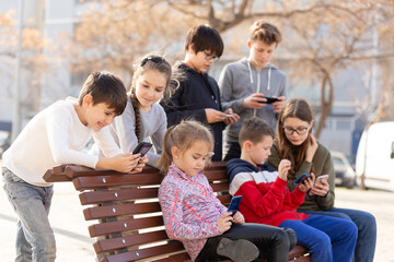 Group of boys and girls addicted in their phones spending time together outdoors