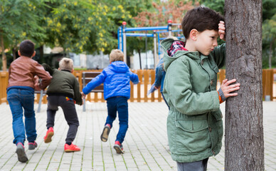 Fototapeta premium Tween boy playing hide and seek with his friends on playground in autumn day..