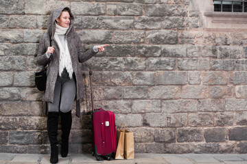 Fototapeta na wymiar cheerful female with baggage in the historical city in hood near wall