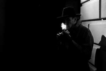 dark dramatic silhouette of a man in a hat Smoking a cigarette on the street at night