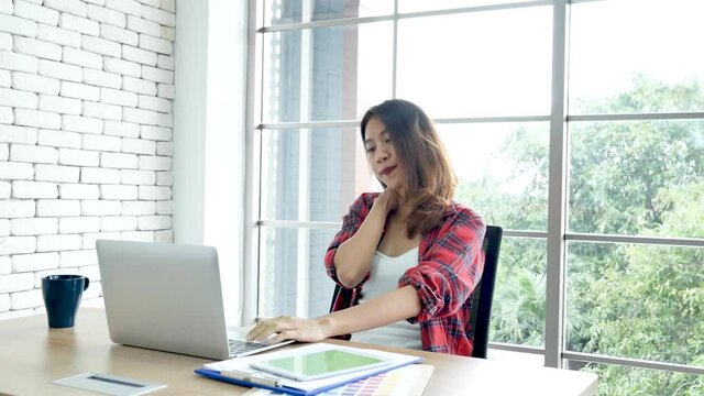 Woman streching arm raised sitting incorrect position home office desk. Back side of young asian woman tired from work body stress back pain office syndrome. Female work from home new normal concept