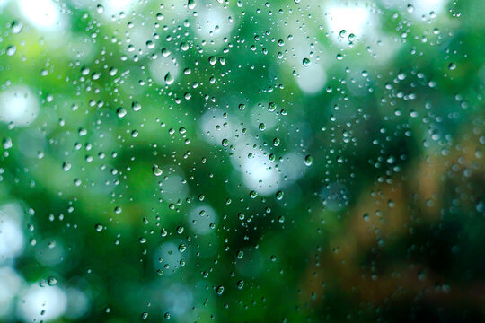 Rain droplets on surface of car glass with blurred green nature background through window glass of car covered by raindrops. Freshness after rain. Wet windscreen shot from inside car. Selective focus. © maemodnit13