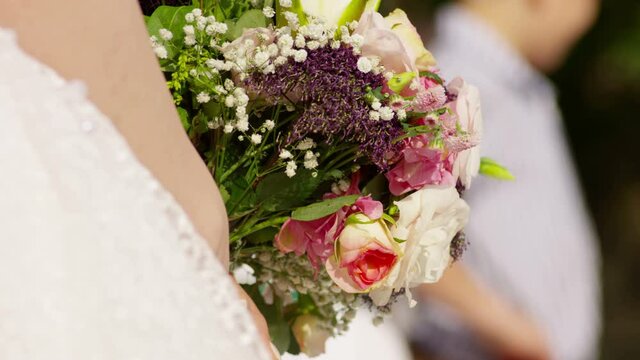 Beautiful bridal bouquet in hands of young bride dressed in white wedding dress. Close up of big bunch of fresh white roses and tulips flowers in female hands . Colorful flower bouquet . Slow Motion .