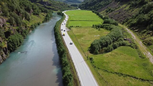 Norway road E39 with traffic passing through idyllic stardalen between Klakegg and Byrkjelo in Sogn - Forward moving aerial following cars on road between river and green fields