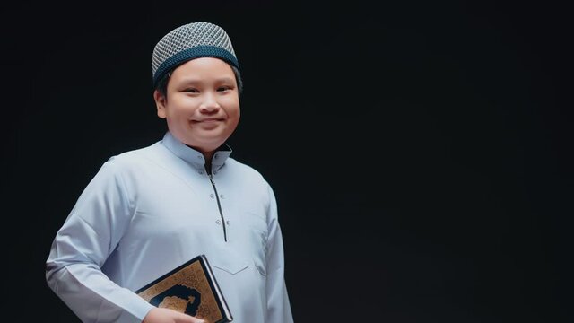 A Muslim boy in Asian Islam is standing and reading the Quran and appreciates on black background,