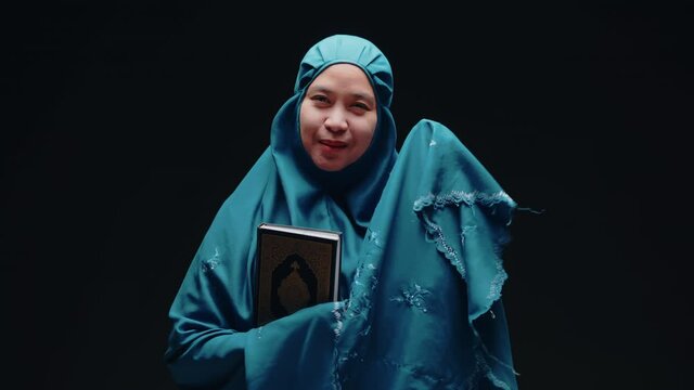 Asian Muslim woman standing and reading the Quran and appreciates and faith The Holy Al Quran with written Arabic calligraphy meaning of Al Quran, Arabic word translation : The Holy Al Quran.