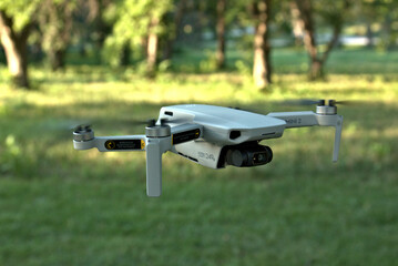 Late afternoon close up of a quad copter flying above the green grass and trees in the background