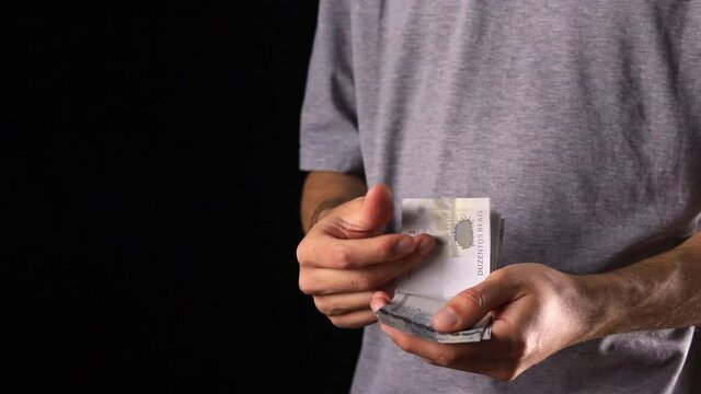 A man counting 200 reais bills on a black background